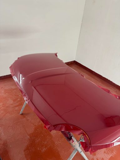 A freshly painted car hood in glossy red placed on a stand in a room.