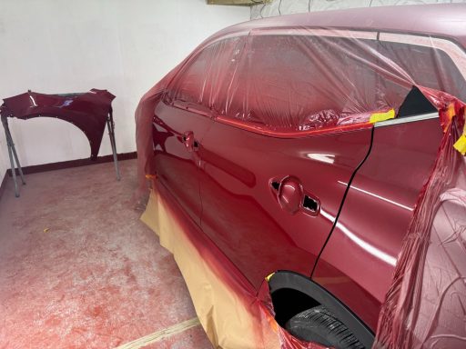 A red car partially covered with protective material in a workshop.